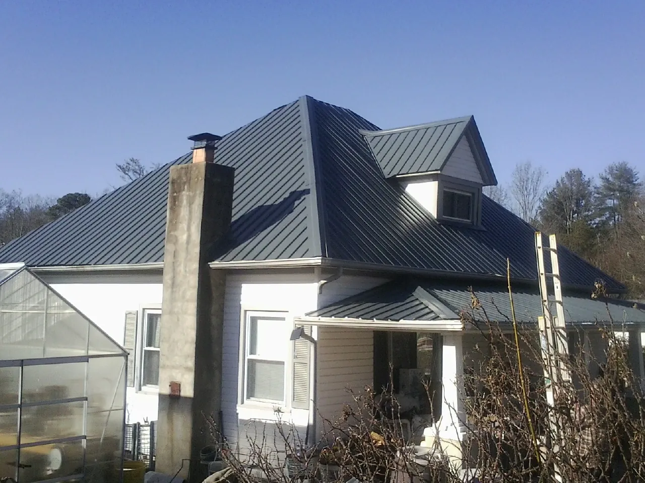 Dark blue standing seam metal roof on a white farmhouse with dormer — Slate & Tile Roof Repair by Roofing Brothers in Colleyville