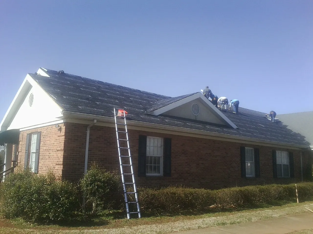 Crew tearing shingles off a brick ranch roof with a ladder set — Emergency Roof Repair work by our crew in Colleyville