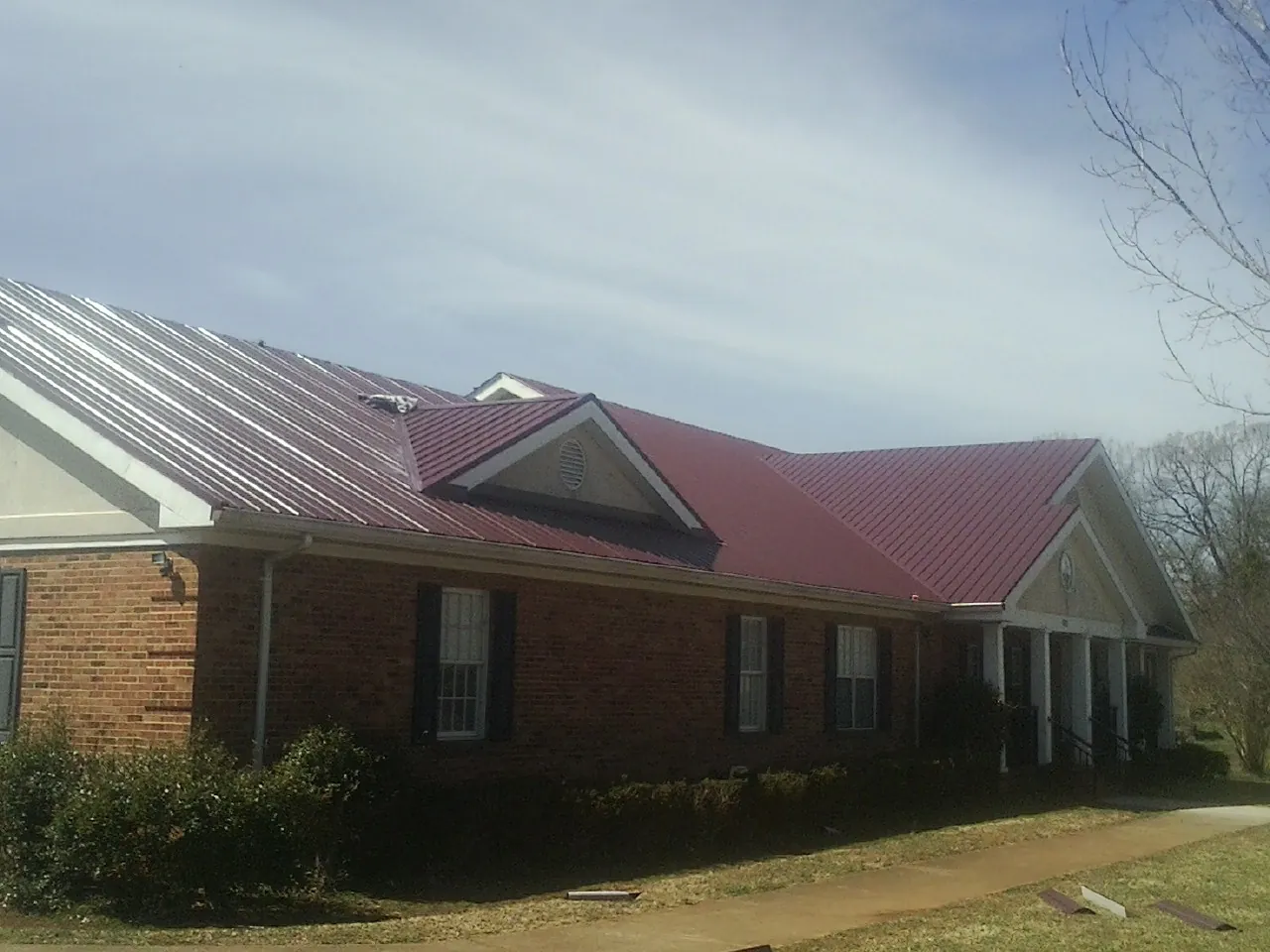 Red metal roof with gabled entries on a long brick building, from a Hail Damage Roof Repair job in Colleyville