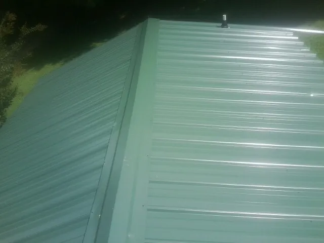 New green metal panels meeting at the ridge of a roof — Flat Roof Repair work by our crew in Colleyville