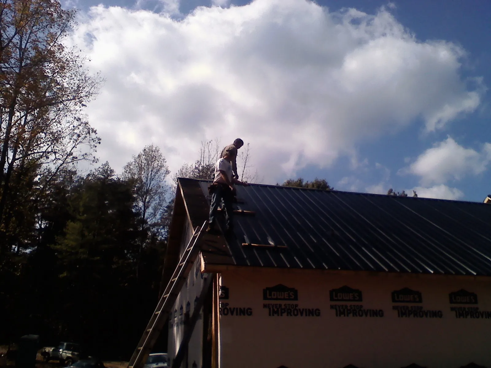 Roofer fastening dark metal panels high against a cloudy sky, from a Roof Inspection job in Colleyville