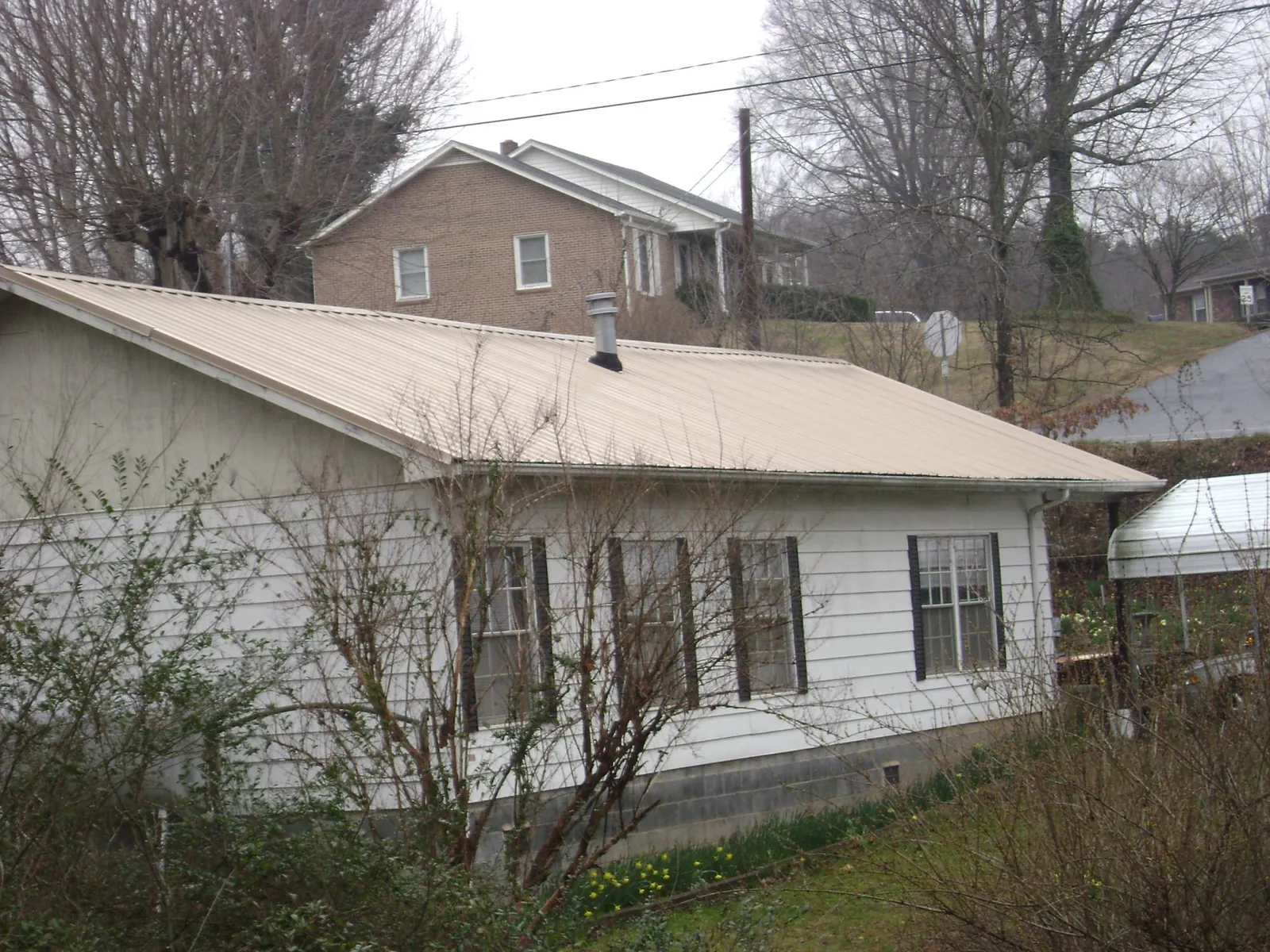 Tan metal roof on a white sided house set into a hillside — Commercial Roofing by Roofing Brothers in Colleyville